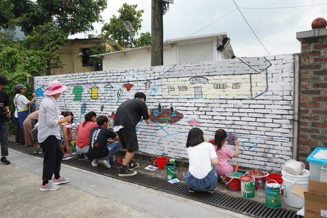 Villagers, artists and students paint a new mural together outside of a residence.